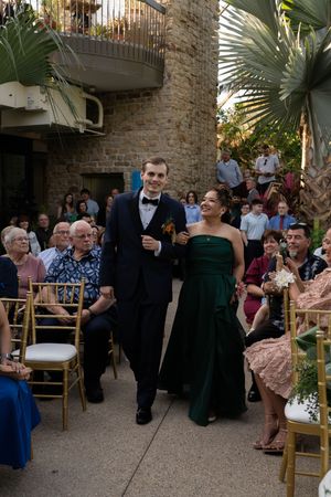 Wedding guests seated on gold chairs in an outdoor venue with brick walls and palm trees.