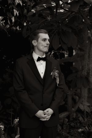A formal portrait of a groom in black tuxedo against garden backdrop.