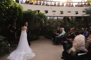 A wedding ceremony in a garden conservatory with string lights and palm trees.