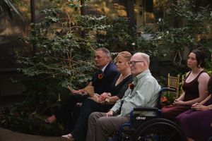 Wedding guests seated in formal attire at an indoor garden ceremony.