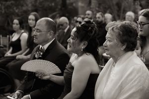Wedding guests holding fans during an indoor ceremony with tropical plants.