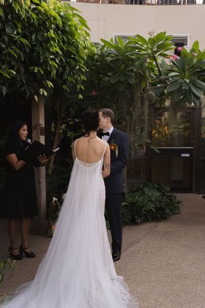 A wedding ceremony takes place in an intimate garden setting with tropical plants.