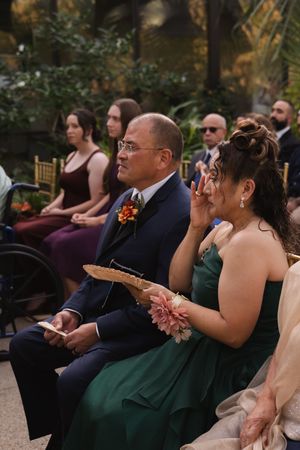Guests in formal attire watch intently during an indoor wedding ceremony.