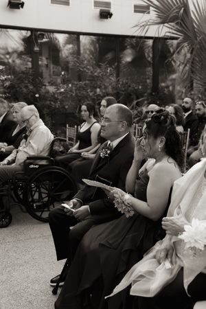 Wedding guests seated in rows beneath palm fronds during an indoor ceremony.