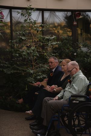 Elderly guests in wheelchairs attend a garden wedding ceremony.