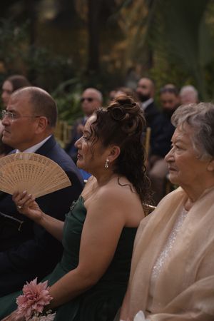 Wedding guests use decorative fans while seated during an indoor ceremony.