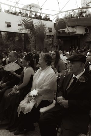 Black and white photo of wedding guests seated under a tent during ceremony.