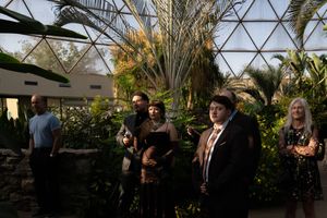 Wedding guests gather in a lush botanical garden setting under a geodesic dome structure.