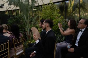 Guests watching a wedding ceremony in a garden conservatory with palm trees.