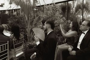 Monochrome shot of wedding guests seated in rows at an indoor garden ceremony.
