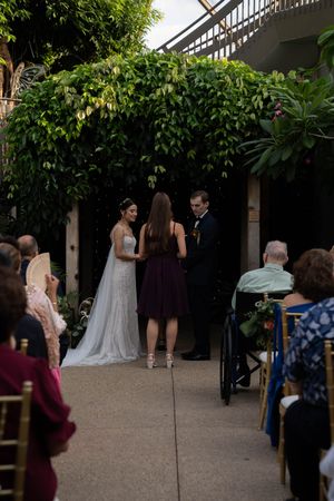 Wedding ceremony procession in a lush garden pathway with guests looking on.