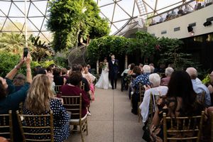 Guests seated in elegant chairs at an outdoor wedding ceremony venue with natural decor.