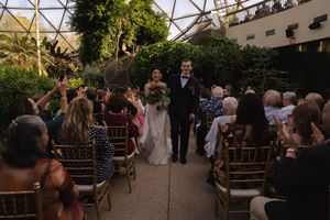 Wedding ceremony guests seated in rows of wooden chairs under a geometric glass dome ceiling.