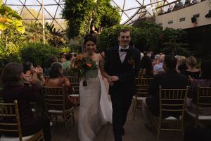 Wedding ceremony space decorated with natural foliage under a modern glass dome structure.