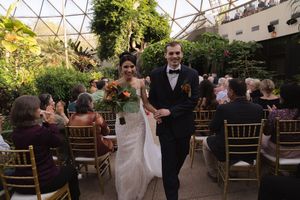 Botanical garden wedding venue with geometric glass roof and rows of elegant gold chairs.
