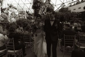 Black and white photo of wedding ceremony in glass-domed conservatory with garden setting.