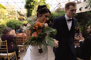 Indoor garden wedding ceremony with guests seated under architectural glass dome ceiling.