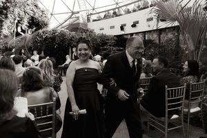 Wedding guests mingle and dance at an outdoor reception under string lights and greenery.