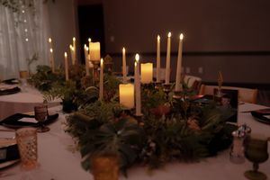 Elegant wedding reception table decorated with candles and greenery in a romantic evening setting.