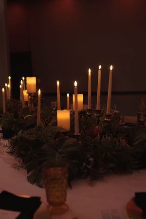 Long table decorated with multiple lit candles and evergreen garland creating a romantic atmosphere.