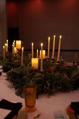 Elegant table centerpiece with glowing taper candles and greenery arrangements creating warm ambient lighting.