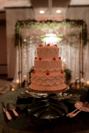 White wedding cake with delicate piping details and red accents displayed on a dark table.