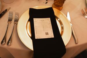 Elegant place setting with black napkin and menu card on gold-rimmed plate.