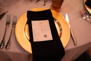 Place setting detail with black napkin and menu card on gold charger plate.