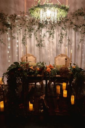 Enchanting sweetheart table with crystal chandelier, greenery, and glowing candles.
