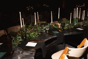 Formal dinner table setting with white candles and greenery decorations in dim lighting.