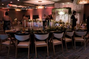 Elegant ballroom setup with round tables and chairs arranged for a formal event under warm lighting and chandeliers.