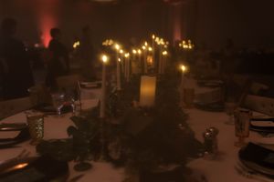 Moody reception table setting with glowing candles and greenery in low light.