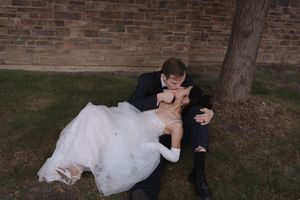 Couple in wedding attire sharing an intimate moment against a brick wall at sunset.