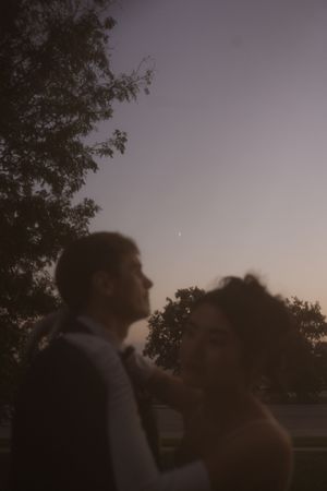 Silhouettes of a couple dancing together at dusk with trees in the background.