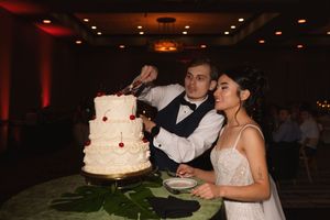 Newlyweds cutting their elegant white wedding cake decorated with red accents.