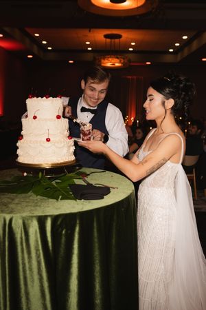 A couple shares a moment while cutting their three-tiered white wedding cake.