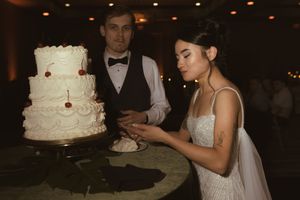 A wedding couple stands next to their elegant white tiered cake at their reception.