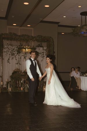 Wedding celebration on a dark dance floor with elegant decor and floral arrangements in the background.
