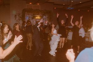 Wedding reception guests dance and celebrate on a crowded dance floor under warm lighting.