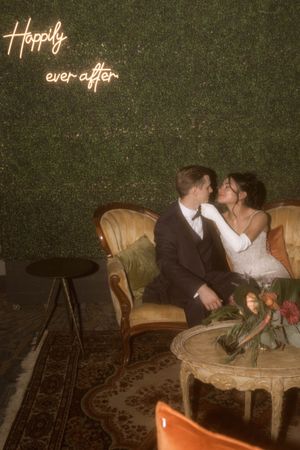 A couple sits together on an antique sofa with 'Happily ever after' text illuminated above.
