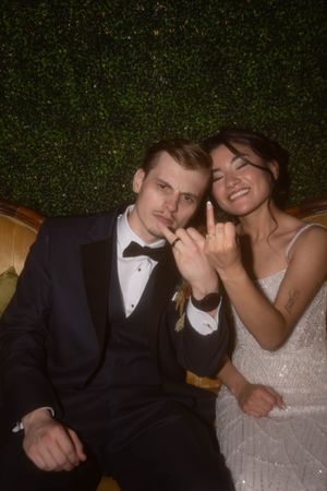 Couple in formal wedding attire sharing playful moments against a green hedge backdrop.