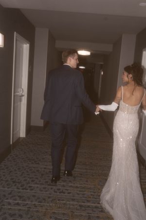 Newlyweds walking down a carpeted hotel hallway after their reception.