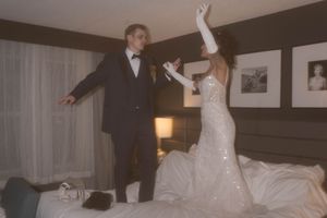 Couple celebrating in a hotel room with champagne and wedding attire.