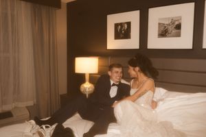 A warm-toned wedding photo showing a couple relaxing on a bed with decorative wall art.