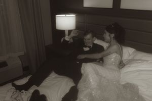 A vintage-style wedding photo of a couple sharing a relaxed moment on hotel bedding.