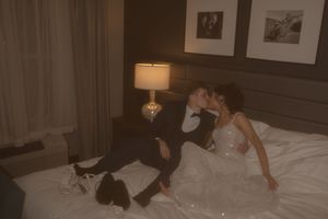 A sepia wedding photograph showing a couple in formal attire relaxing on hotel bedding.