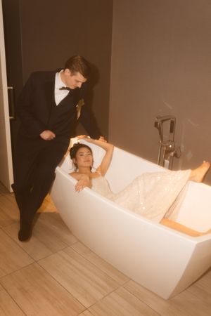 A couple in wedding attire poses dramatically near a modern freestanding bathtub.