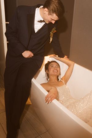A romantic wedding moment captured as a couple shares a playful scene with the bride in a bathtub.