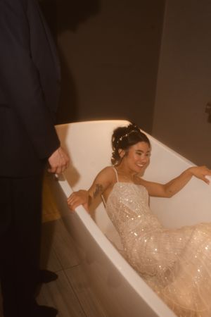 A bride in a sequined gown sits elegantly in a bathtub for a unique wedding photo.