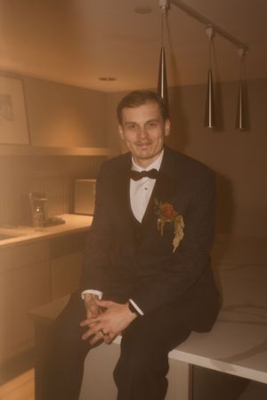 A groom in a tuxedo poses in warm lighting during wedding preparations.
